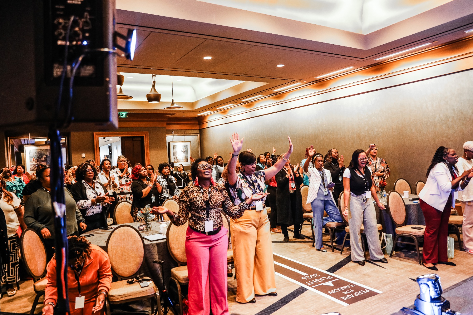 A room of women builders at Pivot 2025 with hands raised in worship
